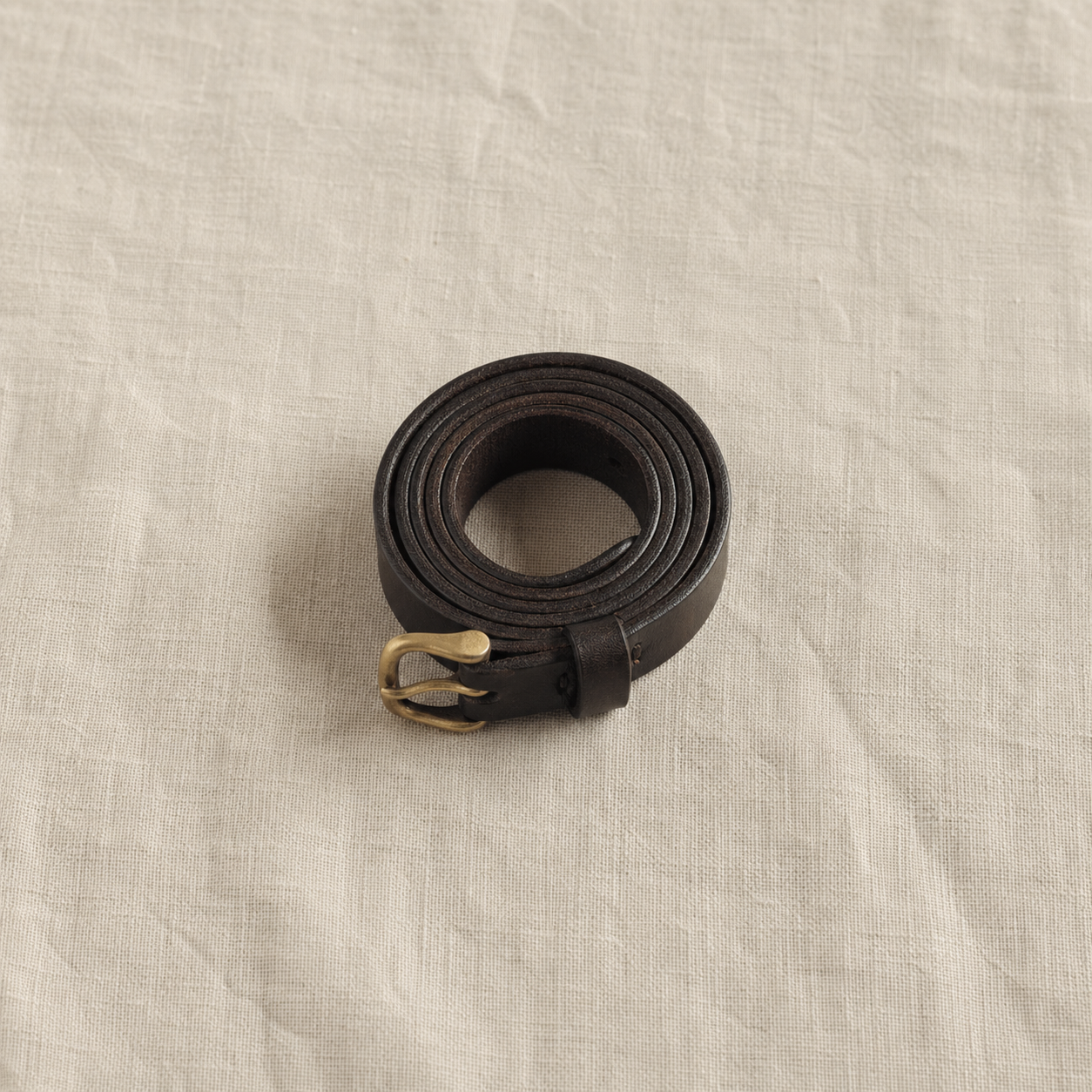棕黑色窄版牛皮皮帶捲起置於亞麻布上